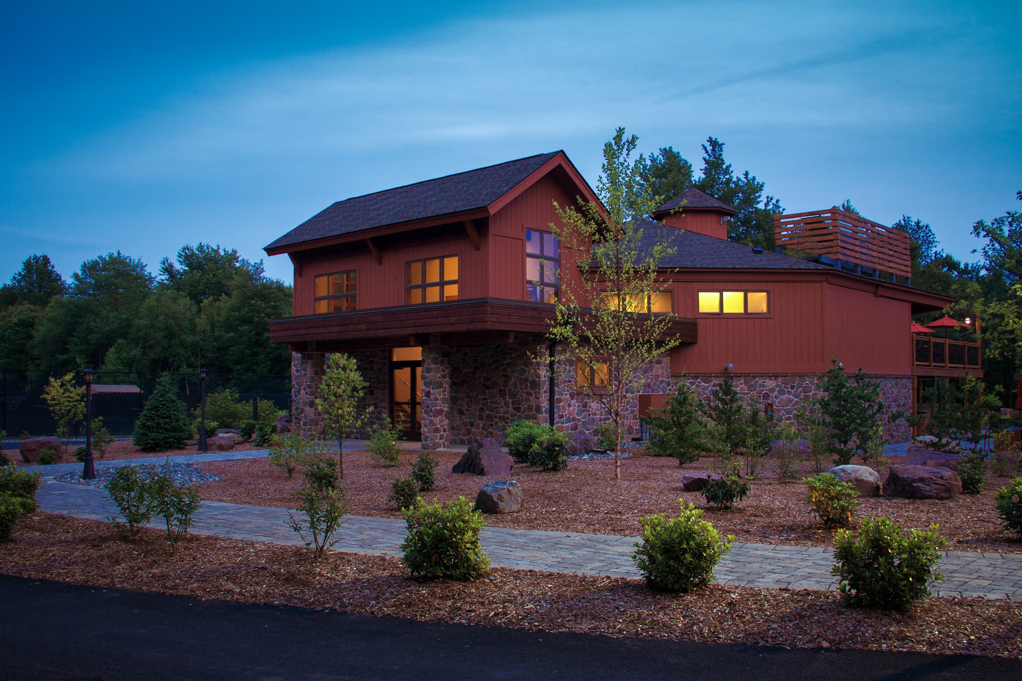 A modern two-story house with stone accents and landscaped surroundings at dusk.