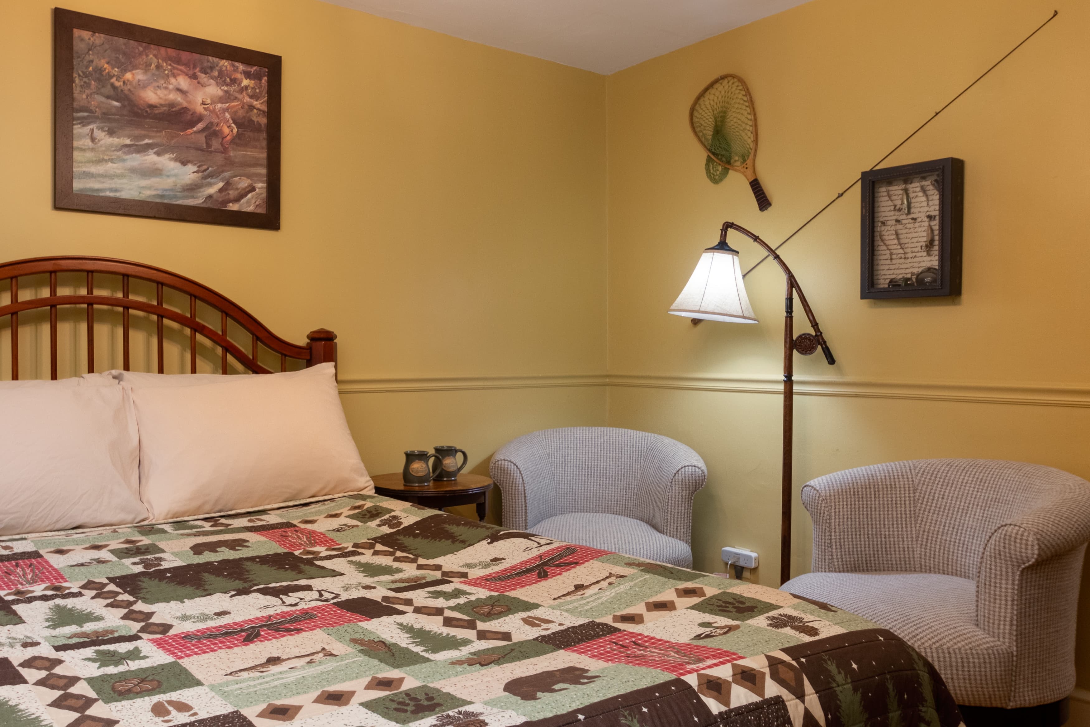 A cozy bedroom with a wood-spindle headboard, a bear and tree-themed quilt, and two small white armchairs against bright yellow walls.