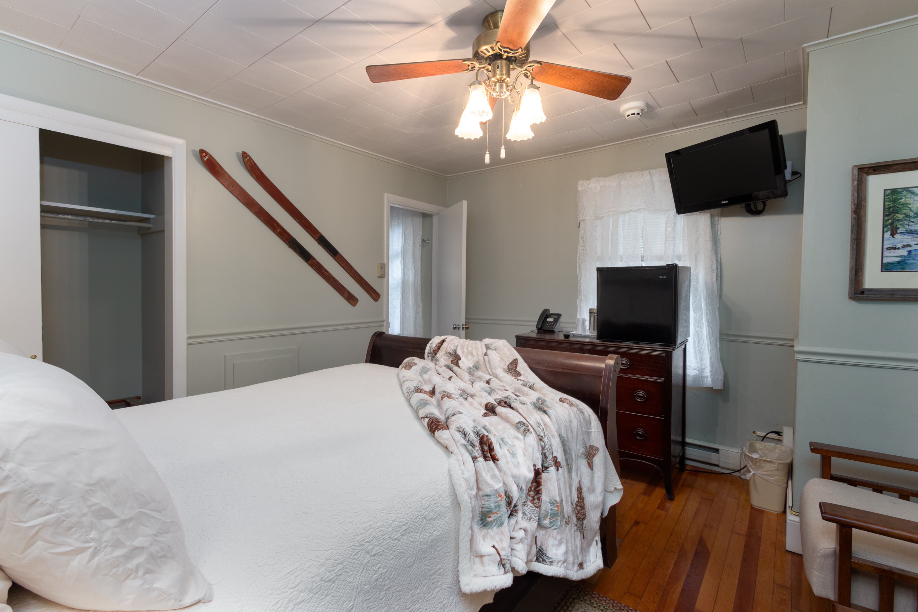 A cozy bedroom with light green walls, a dark wood bed, and hardwood floors, featuring vintage wooden skis as wall decor.