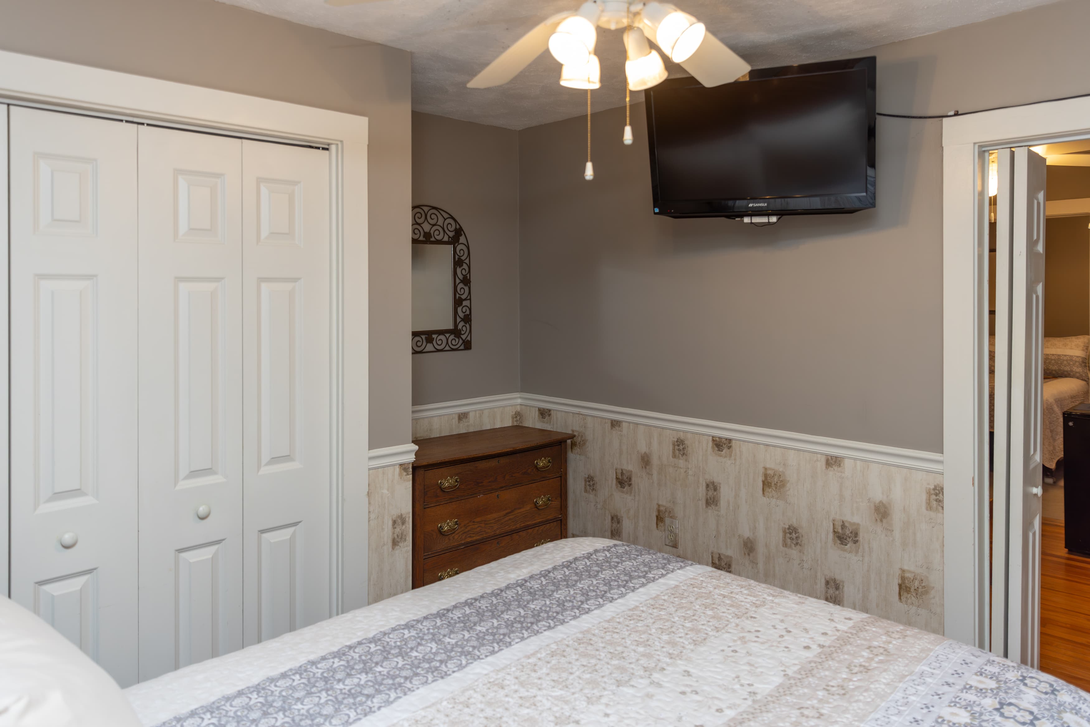 A bedroom with a dark wood dresser against a two-toned gray and patterned wall, featuring a wall-mounted TV and a closet.