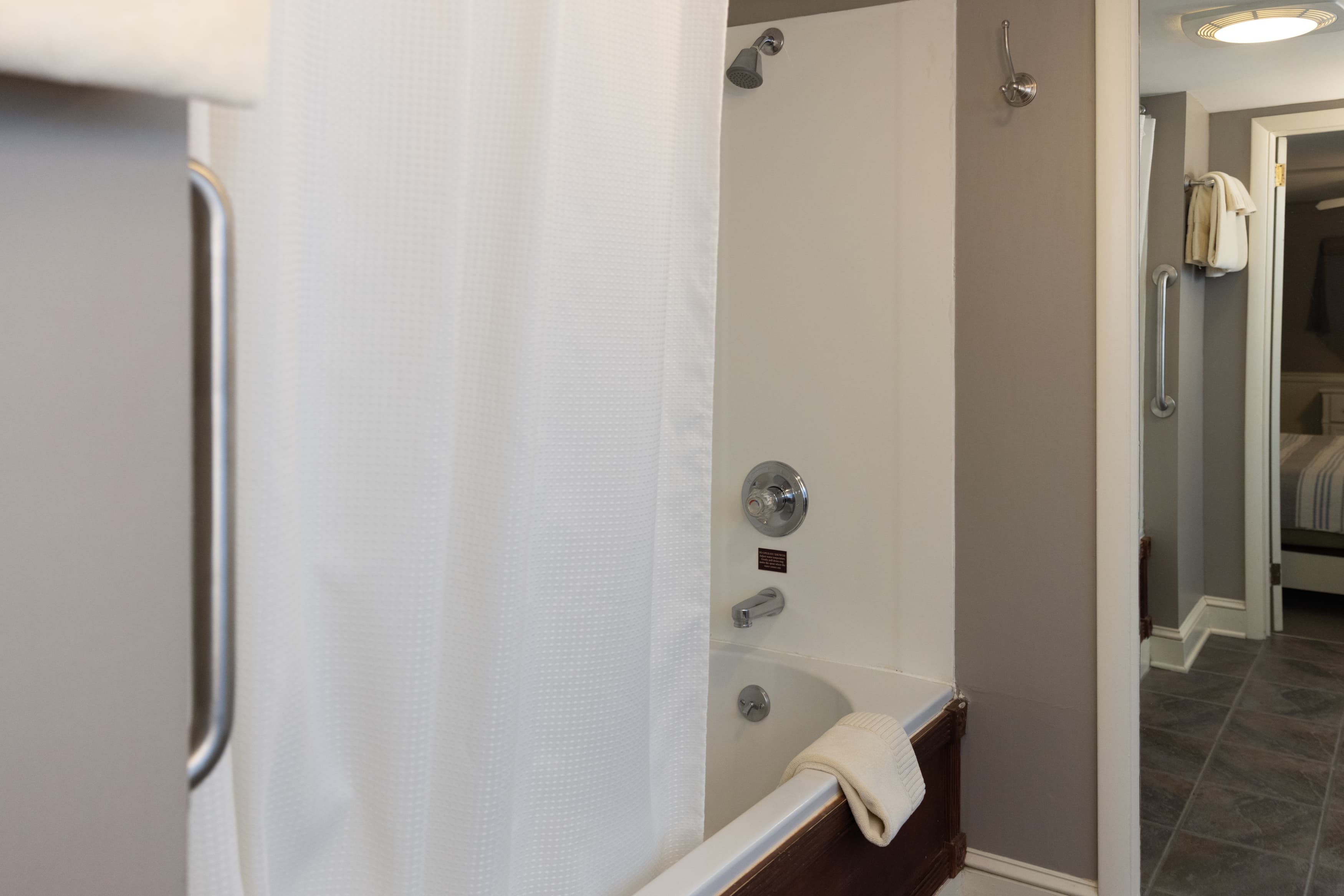 A close-up of a clean, white bathtub/shower combo with a white curtain and brushed nickel fixtures in a gray-walled bathroom.