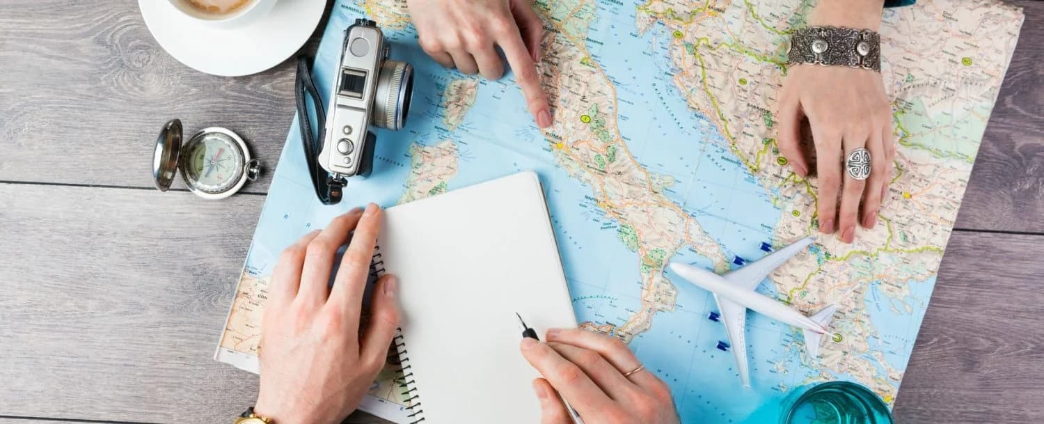 Two people planning a trip using a map, notebook, and camera on a wooden table.