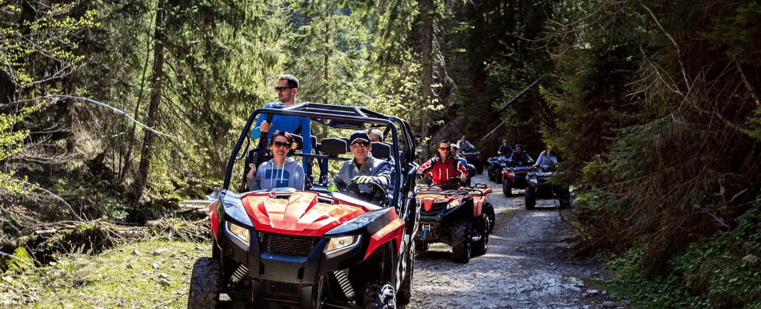A group of people riding all-terrain vehicles on a wooded trail.