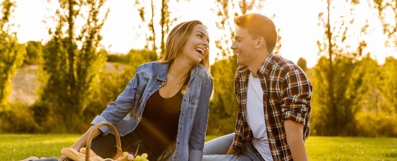 A couple enjoys a joyful moment together on the grass, illuminated by warm sunlight.