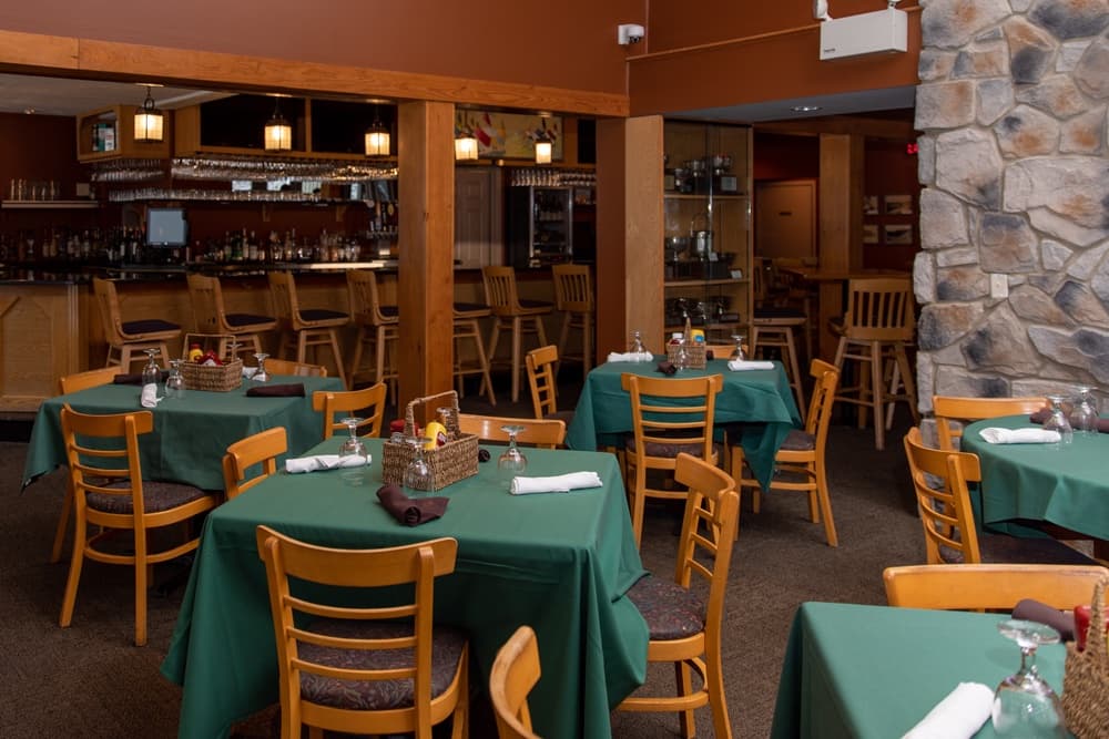 A cozy restaurant interior with green tablecloths and a wooden bar in the background.
