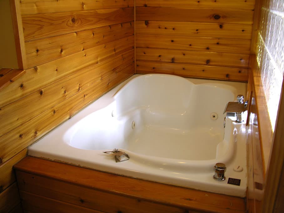 A close-up of a white corner jetted tub set in a wood-paneled alcove with natural knotty pine walls, creating a cozy, rustic spa feel.
