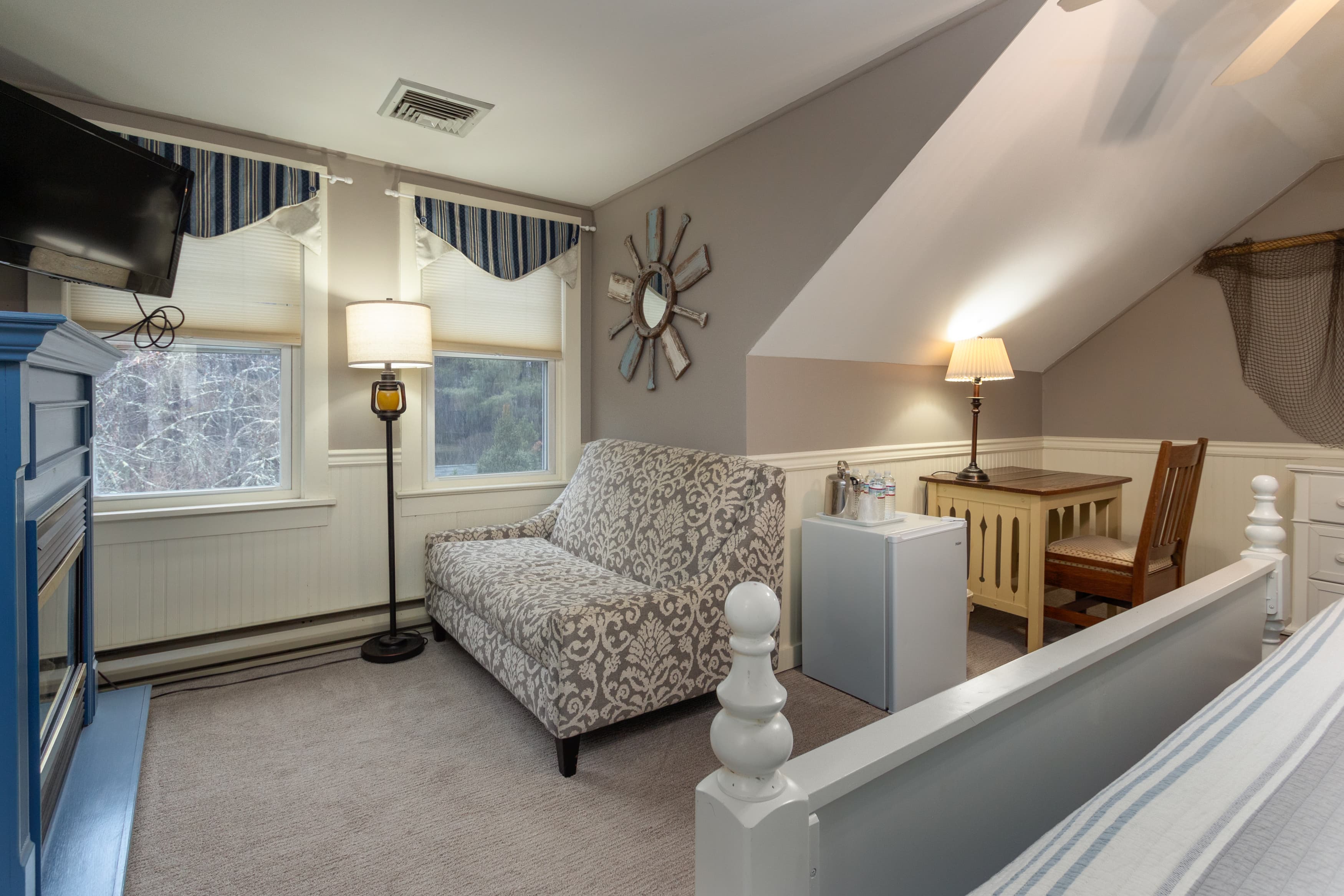 A cozy third-floor suite with a sloping roof, a blue fireplace, a patterned loveseat, and a desk, decorated with a starburst mirror.