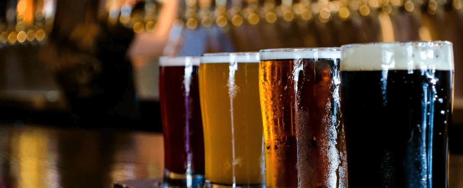A row of five different craft beers in glasses on a bar countertop. A row of five different craft beers in glasses on a bar countertop.