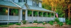 A large, two-story house with a wraparound porch and American flag in a lush, green setting.