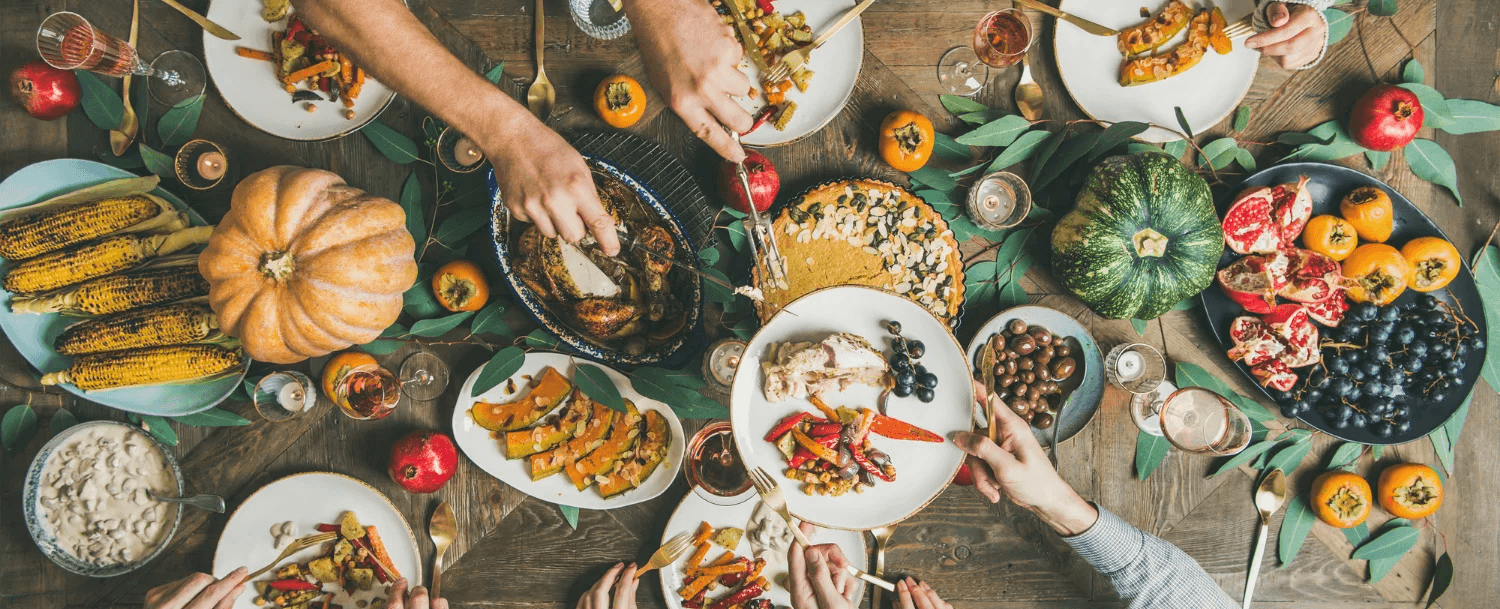 A richly arranged table featuring various autumn dishes, fruits, and hands serving food.