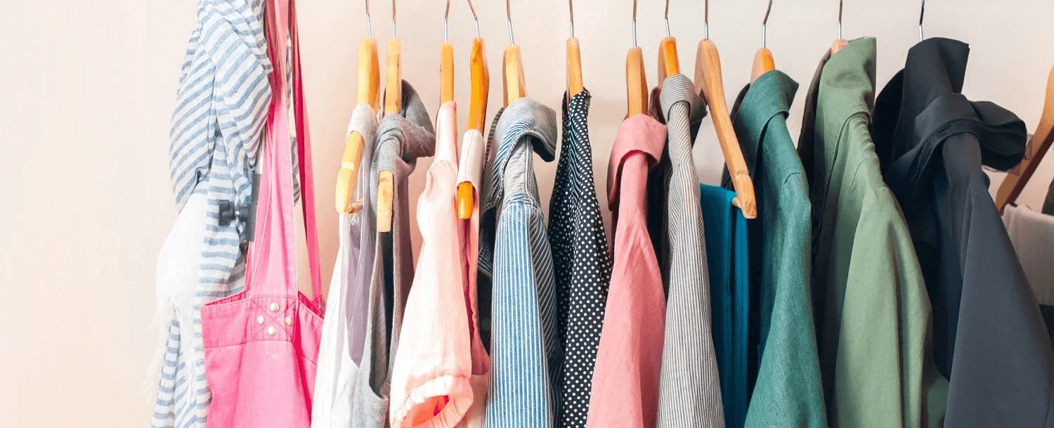 A colorful assortment of clothing hanging on wooden hangers against a pale wall. A colorful assortment of clothing hanging on wooden hangers against a pale wall.
