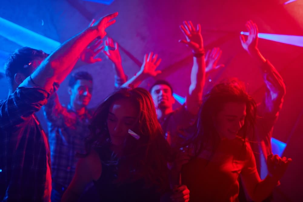 A group of people dance energetically under vibrant blue and pink lights.