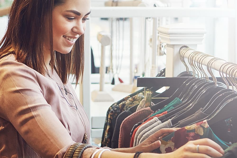 A young woman smiles while browsing a rack of clothes in a stylish boutique.