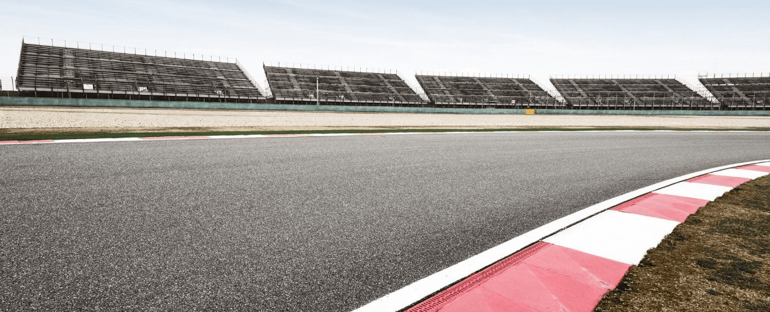 A racetrack curves with empty grandstands in the background under a clear sky. A racetrack curves with empty grandstands in the background under a clear sky.