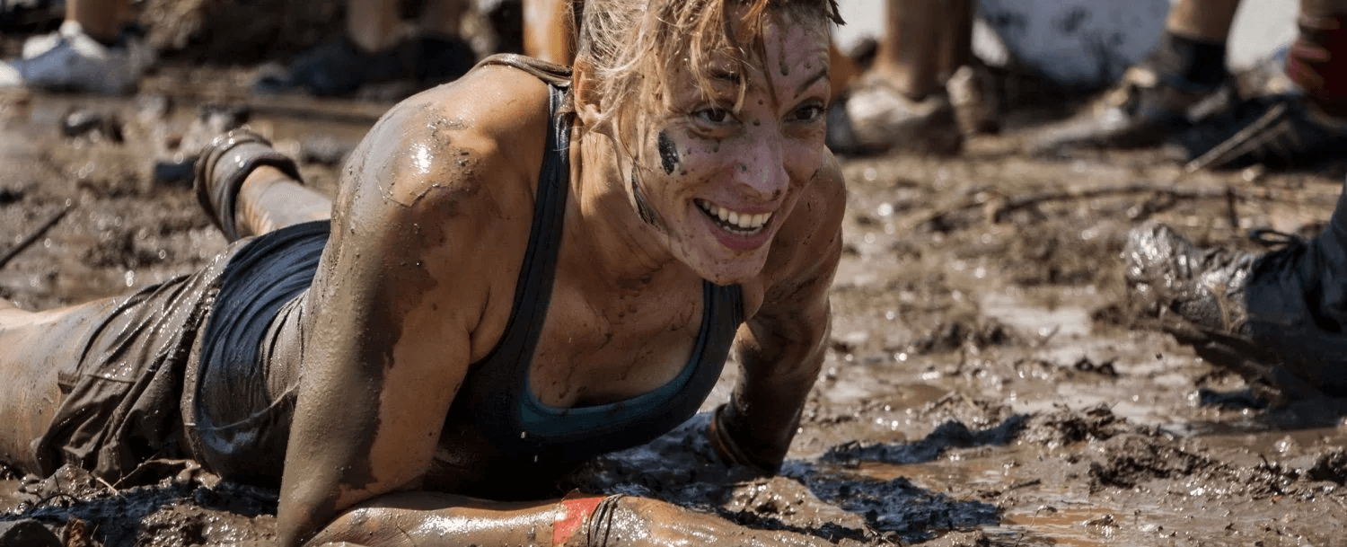 A muddy participant smiles while crawling through a dirt-covered obstacle course. A muddy participant smiles while crawling through a dirt-covered obstacle course.