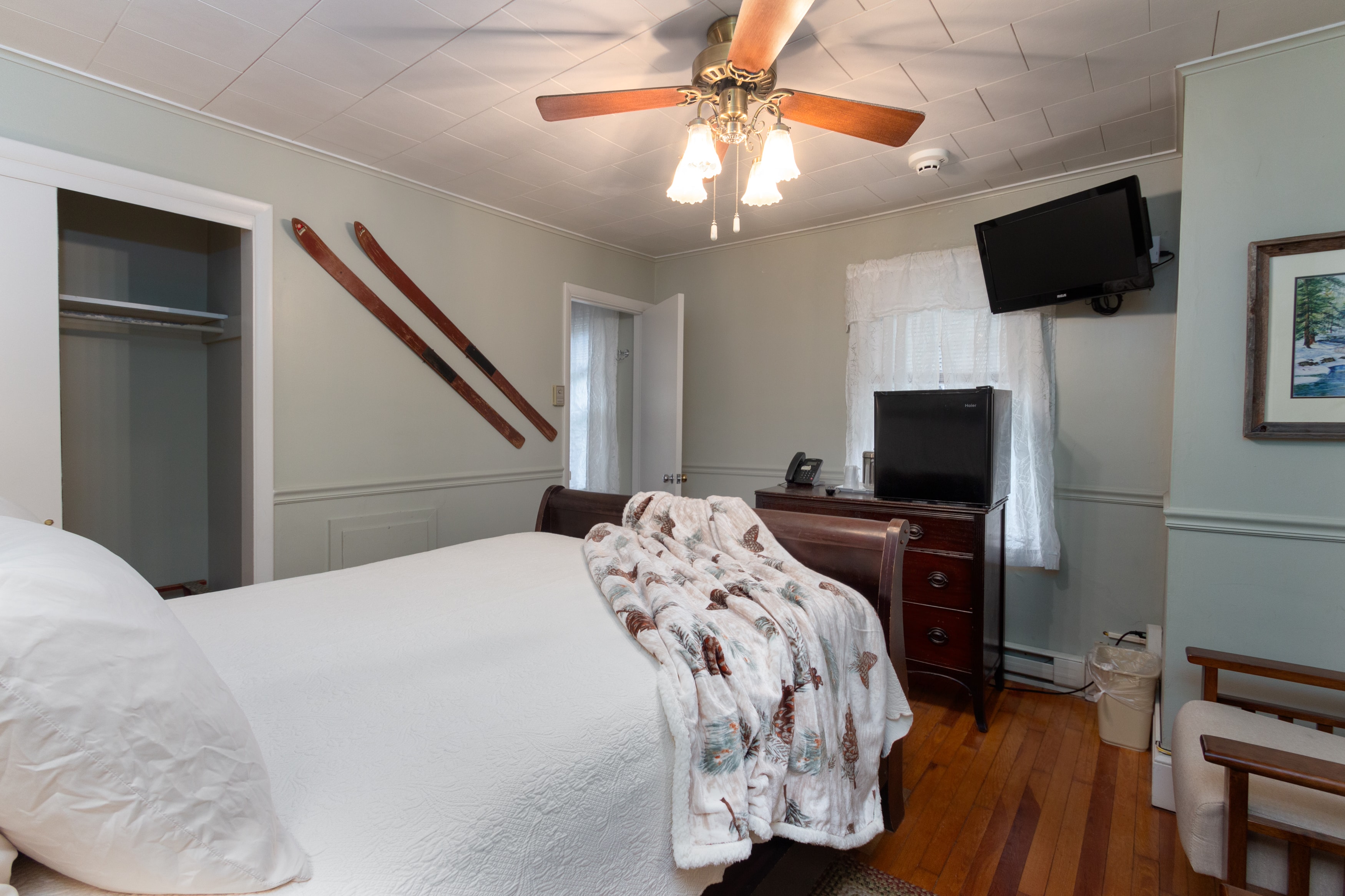 A cozy bedroom with light green walls, a dark wood bed, and hardwood floors, featuring vintage wooden skis as wall decor.