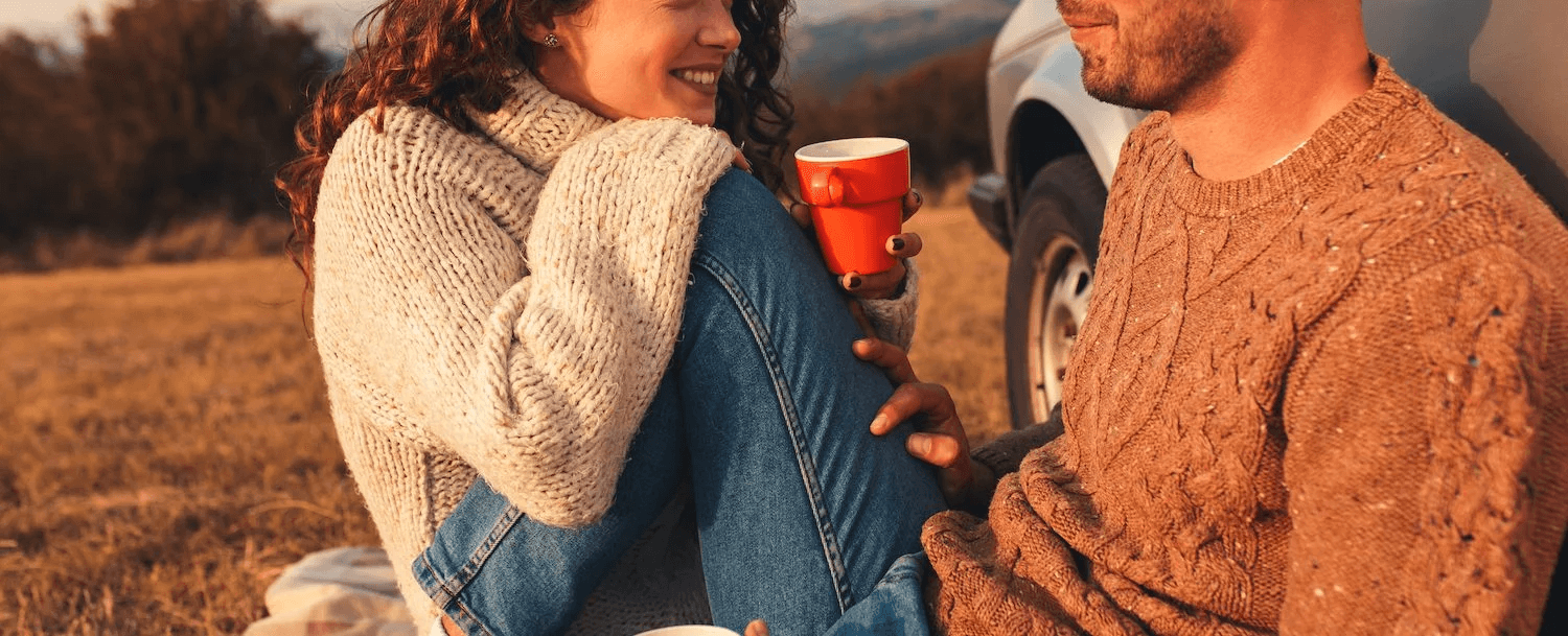 A couple enjoys a cozy moment together outdoors, holding cups and smiling.