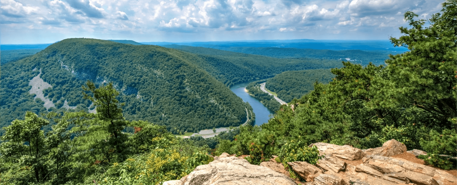 A panoramic view of a lush valley with a winding river and rolling hills under a partly cloudy sky. A panoramic view of a lush valley with a winding river and rolling hills under a partly cloudy sky.