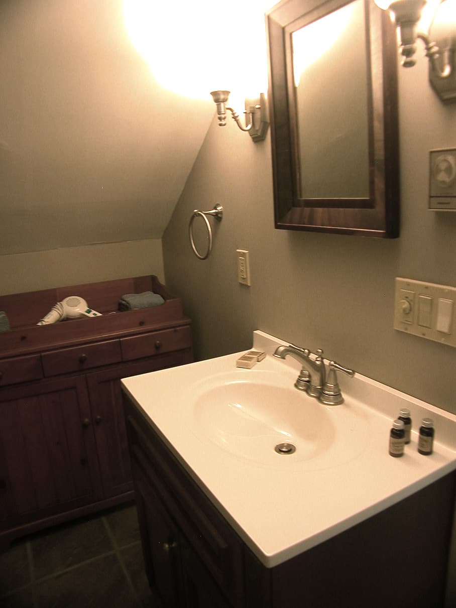 A bathroom with a dark wood vanity and a white countertop, featuring a framed mirror and a separate wooden storage cabinet.