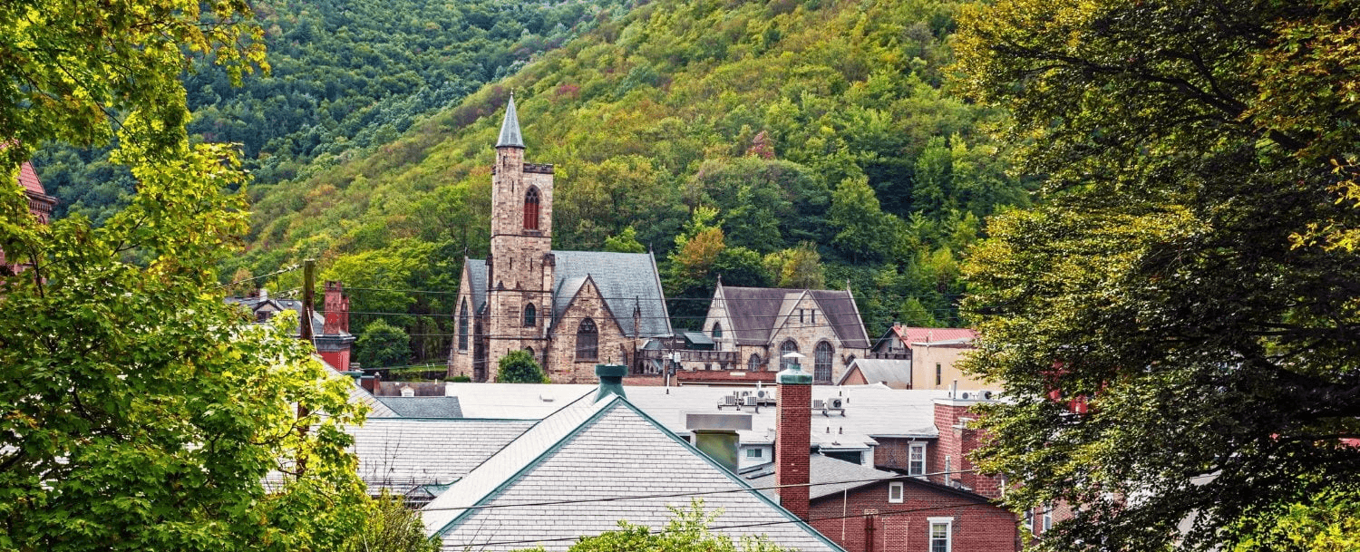 A church tower stands amidst a backdrop of rolling green hills and urban rooftops.