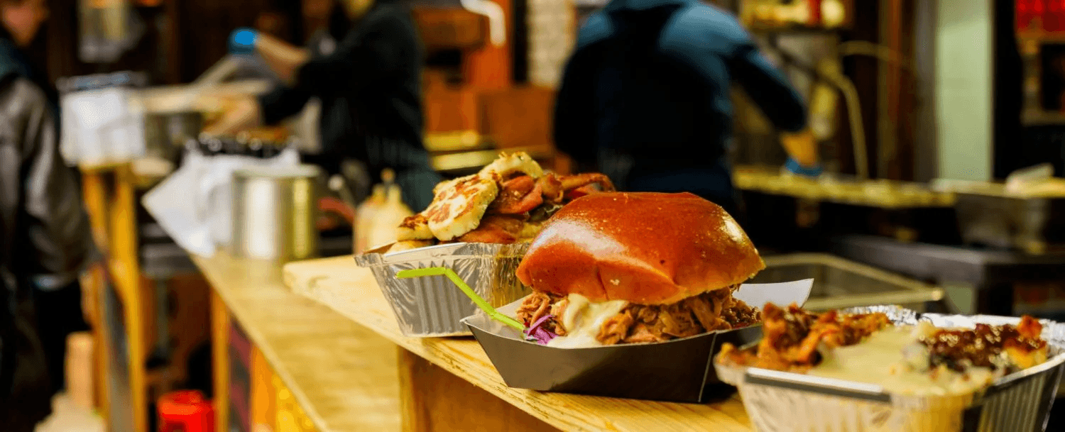 A selection of gourmet sandwiches on a wooden counter in a bustling food stall.