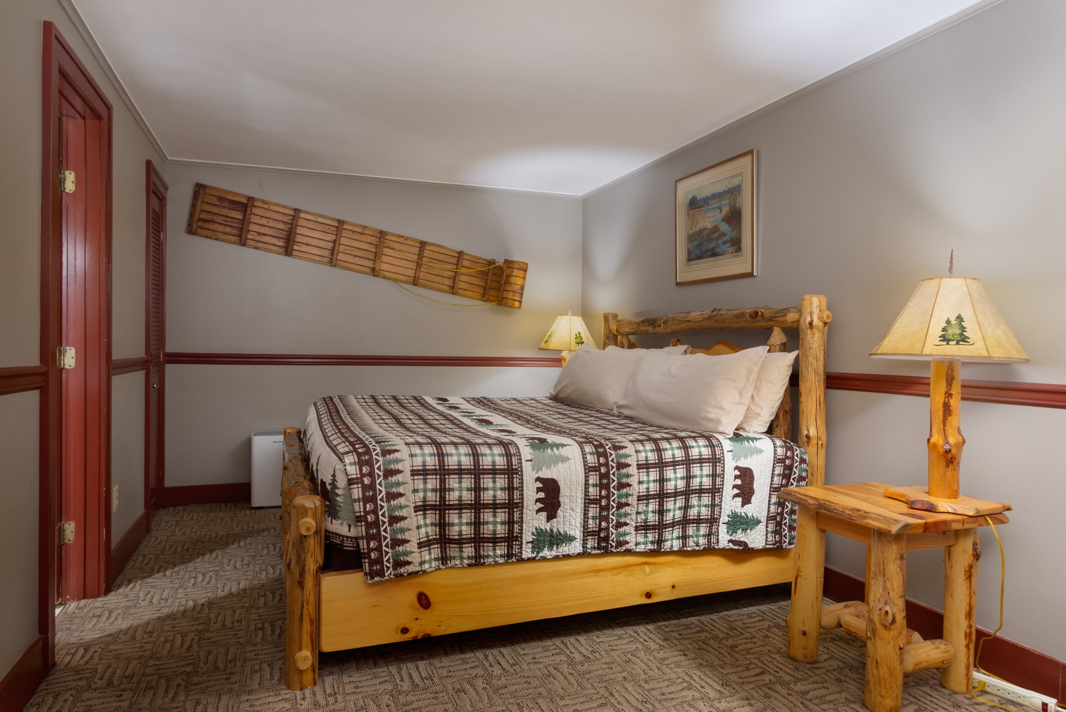 A cozy rustic bedroom with a log-style bed, a bear-themed quilt, and a wooden plank shelf mounted on the wall.