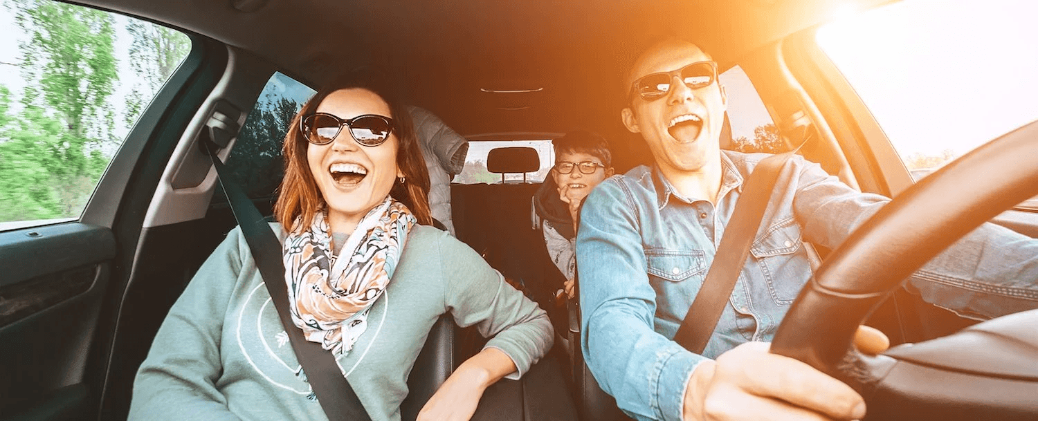Three people in sunglasses joyfully laughing inside a car.