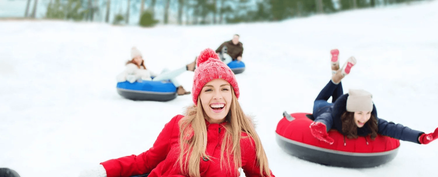 A group of friends enjoys snow tubing on a snowy hill, smiling and having fun.