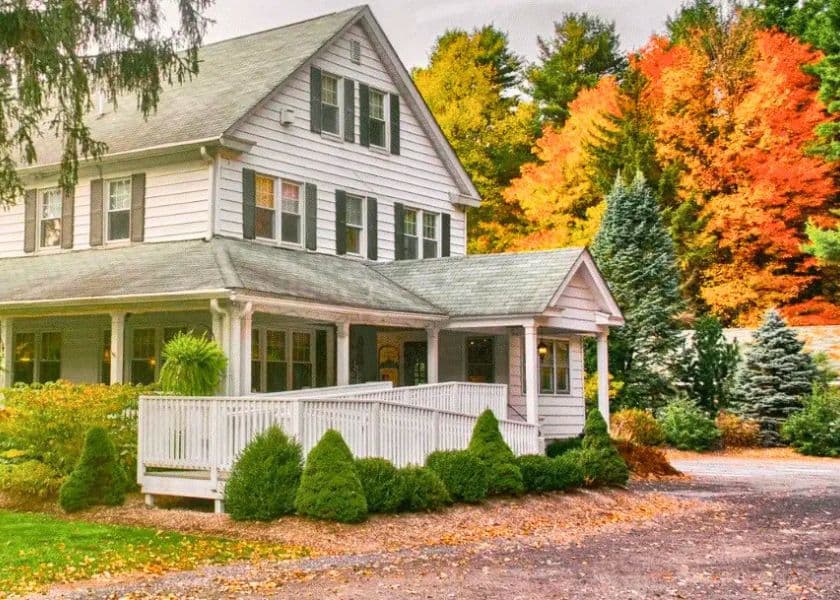 A white two-story house surrounded by colorful autumn foliage. A white two-story house surrounded by colorful autumn foliage.