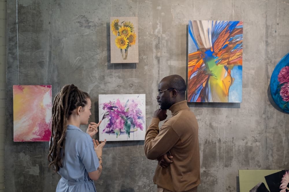 Two individuals engage in conversation about artwork displayed on a gallery wall.