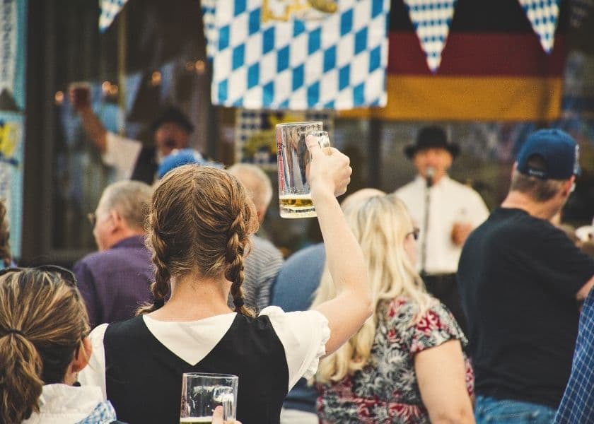 A crowd enjoys a festive event, with a woman in traditional attire raising a beer mug. A crowd enjoys a festive event, with a woman in traditional attire raising a beer mug.