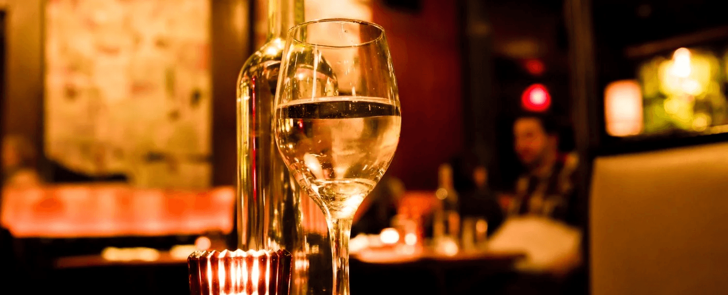 A close-up of a wine glass and bottle in a dimly lit restaurant setting. A close-up of a wine glass and bottle in a dimly lit restaurant setting.