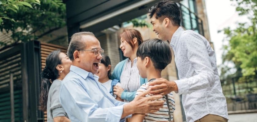 A joyful family gathering with an elderly man embracing a young boy while others smile and engage nearby.