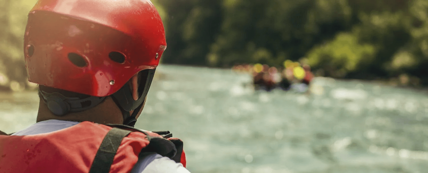 A person in a red helmet watches a group of canoeists on a river.