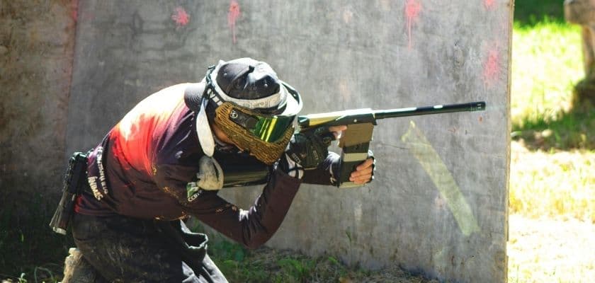 A person in paintball gear takes aim behind a barrier.