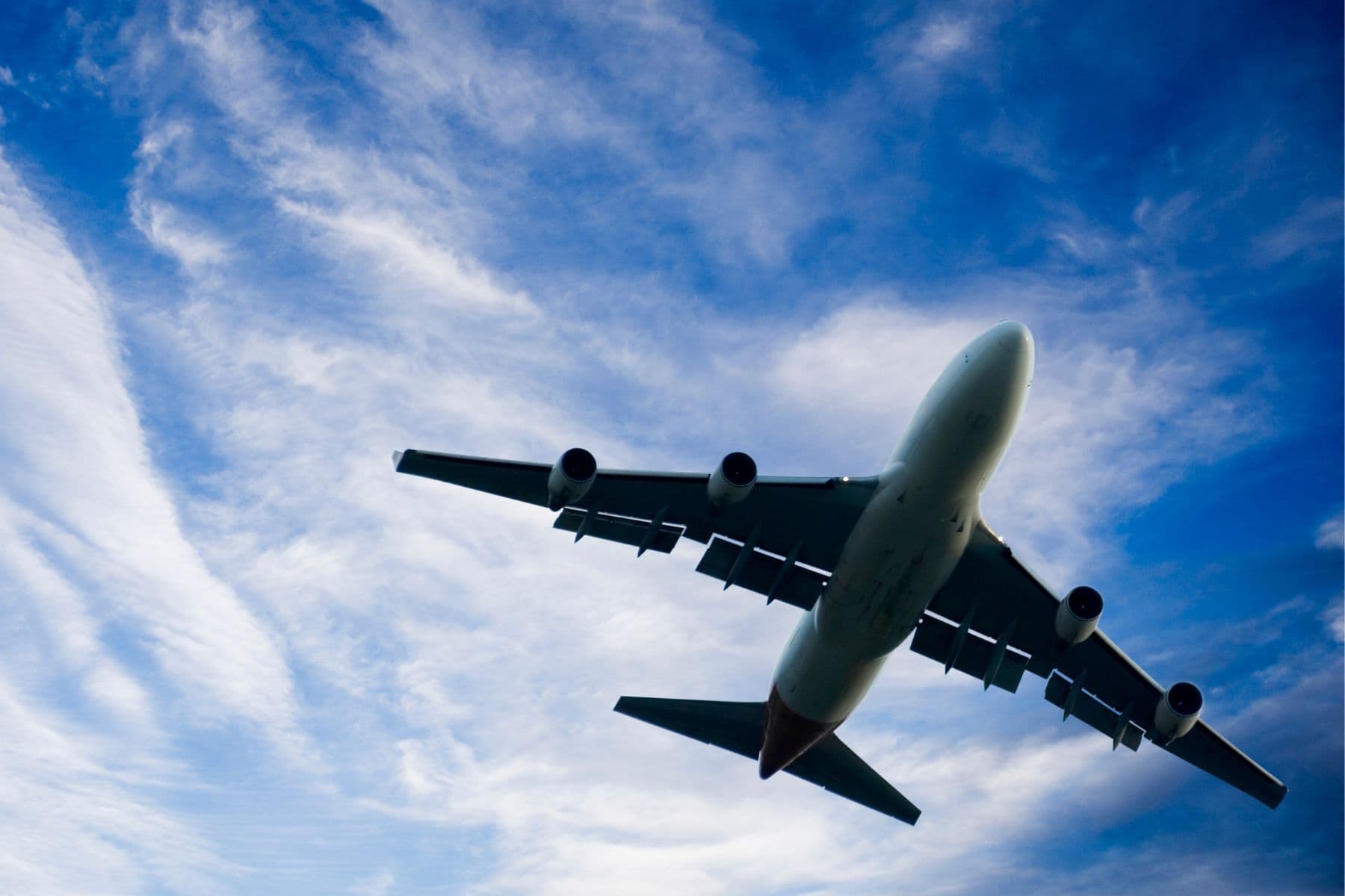 A large airplane flying against a backdrop of blue sky and wispy clouds.