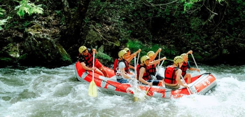 A group of people in helmets paddles a raft through turbulent waters.