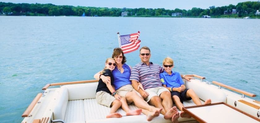A family of four relaxing on a boat with an American flag in the background.