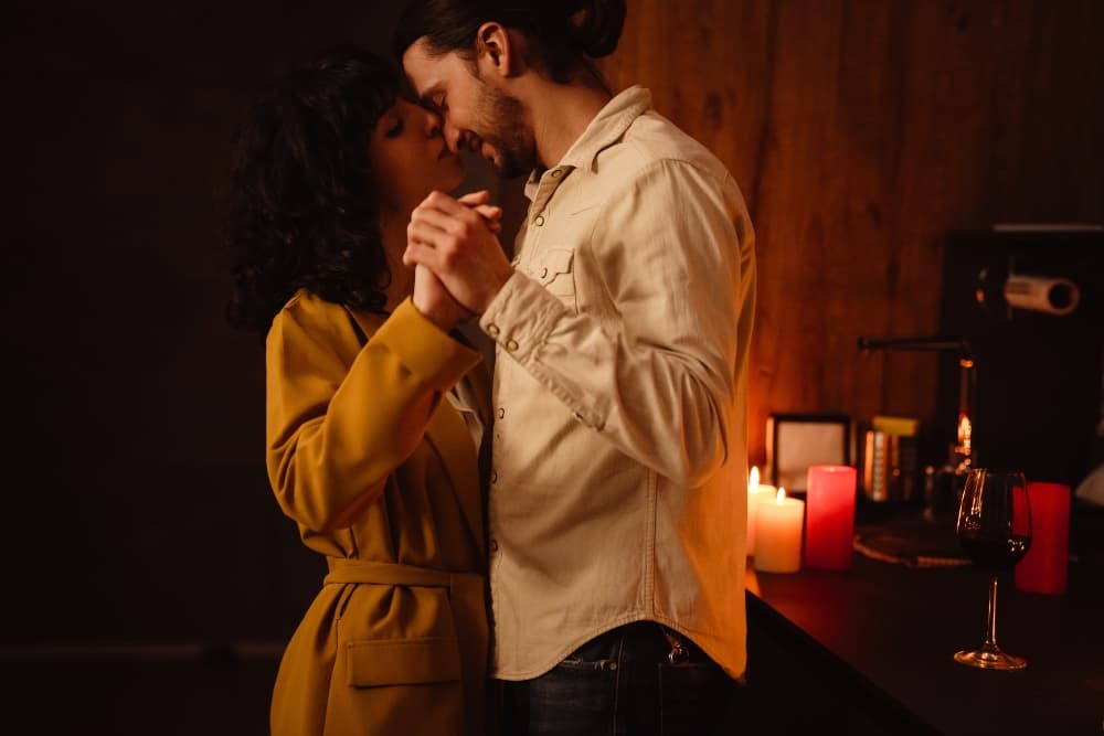 A couple shares a romantic moment while dancing closely in a dimly lit room adorned with candles.