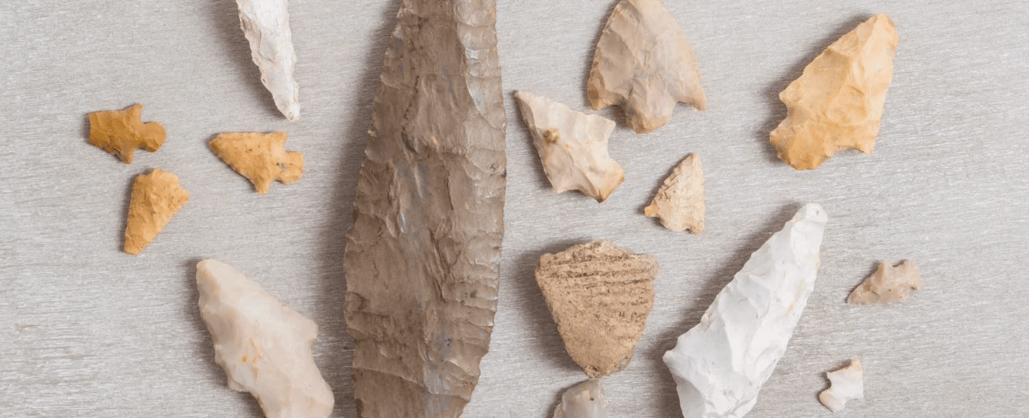 A collection of various stone tools and arrowheads arranged on a light surface. A collection of various stone tools and arrowheads arranged on a light surface.