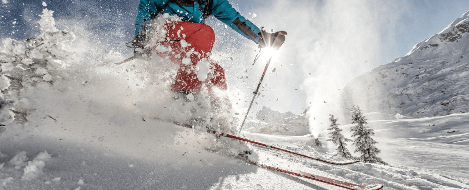 A skier carves through fresh powder snow on a bright, sunny day.