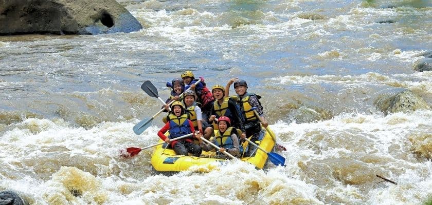 A group of ten people joyfully rafting on a turbulent river.