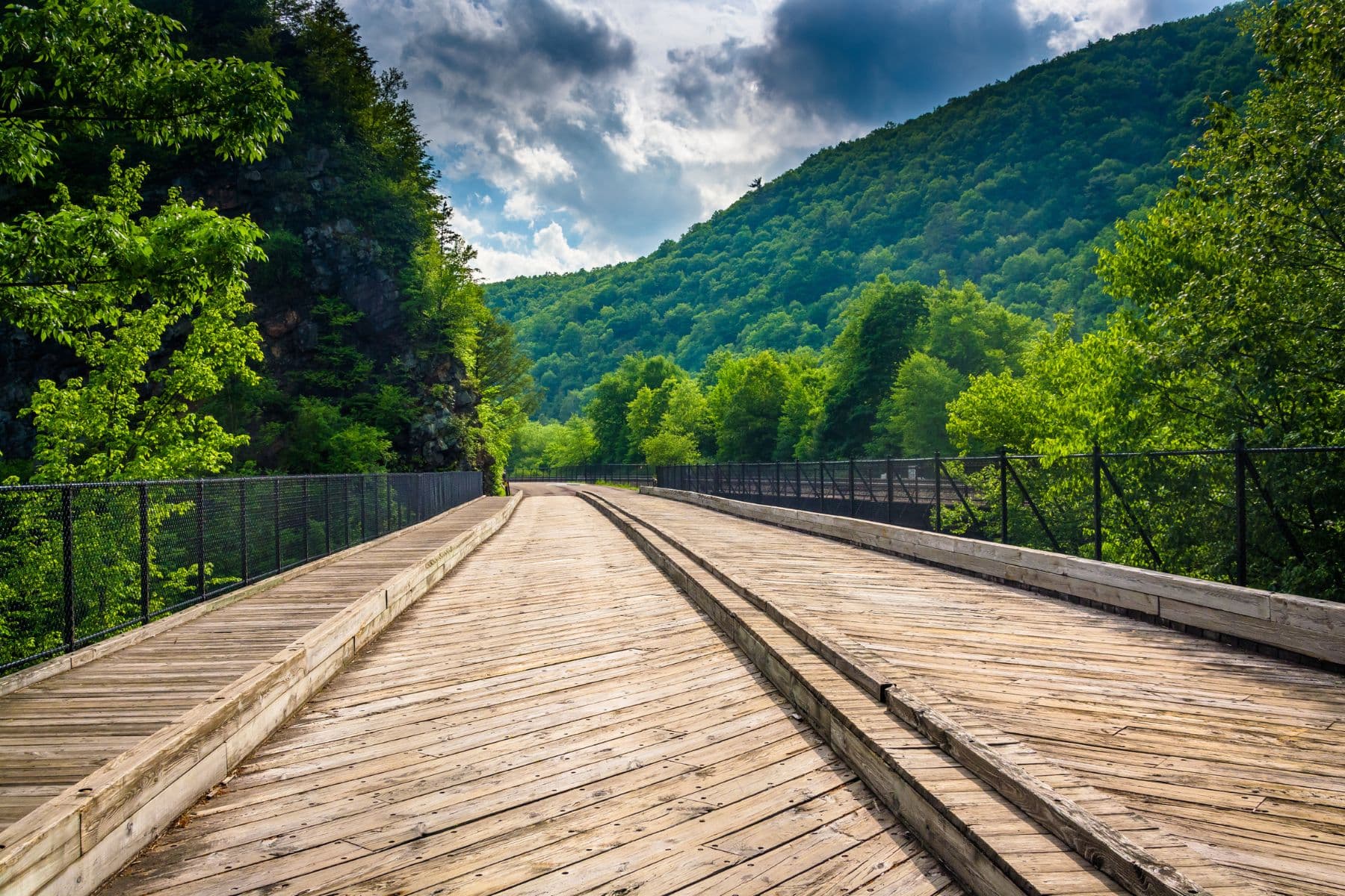 A wooden pathway stretches through lush green hills under a partly cloudy sky. A wooden pathway stretches through lush green hills under a partly cloudy sky.