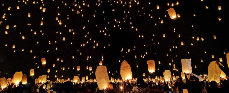 A night sky filled with glowing lanterns released by crowds during a celebration.