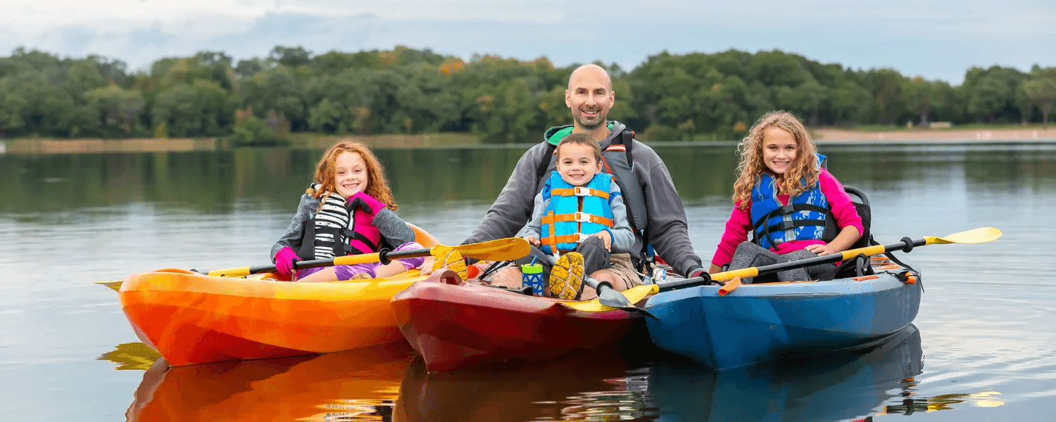 A man and two children are kayaking on a calm lake.