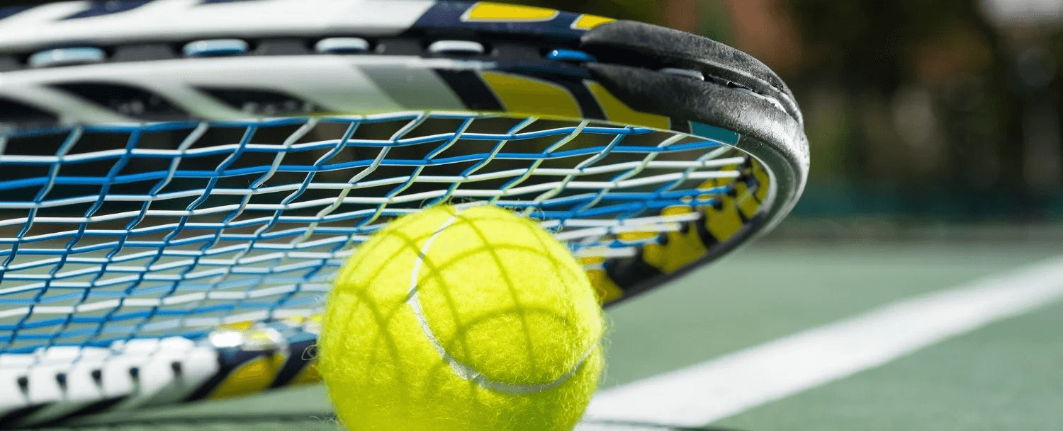 A close-up of a yellow tennis ball resting near a tennis racket on a court.