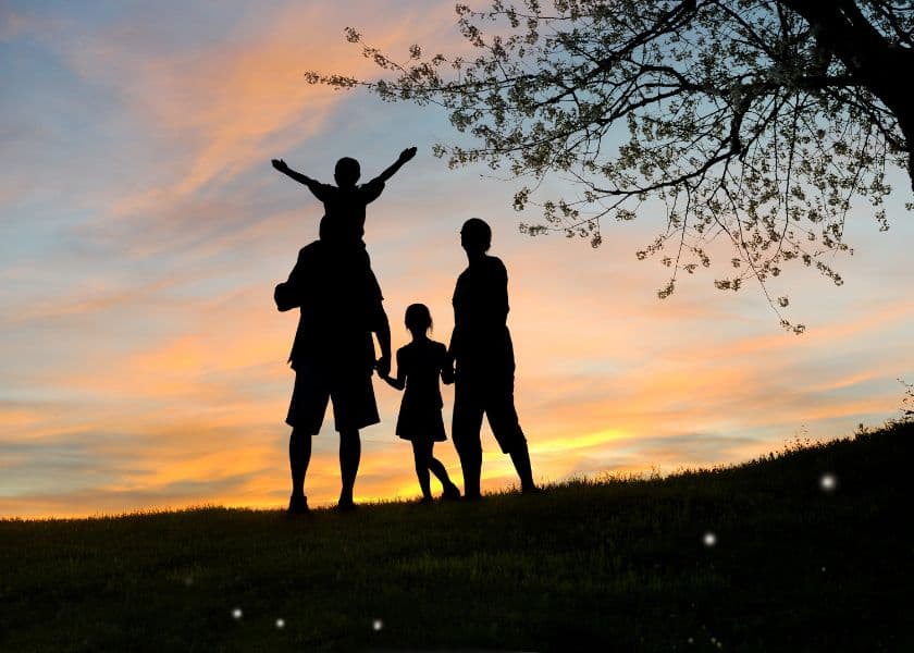 A silhouetted family enjoys a sunset, with one child on an adult's shoulders. A silhouetted family enjoys a sunset, with one child on an adult's shoulders.