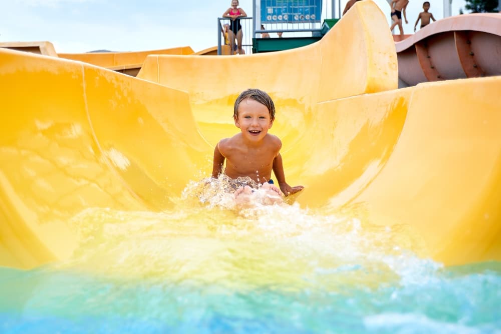 A smiling child splashes down a yellow water slide.