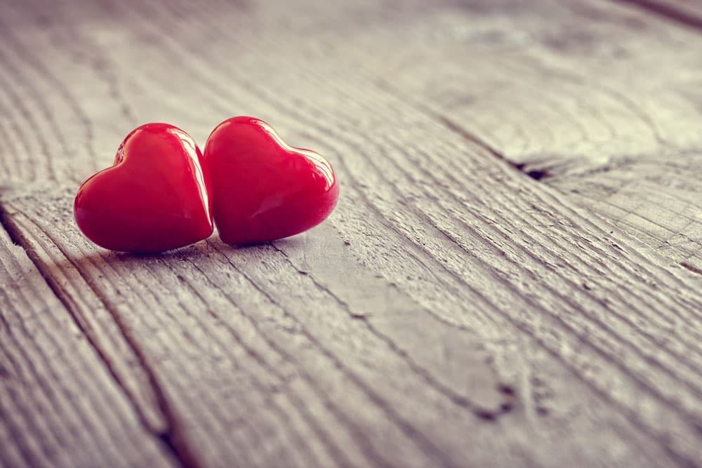 Two glossy red heart shapes resting on a wooden surface.