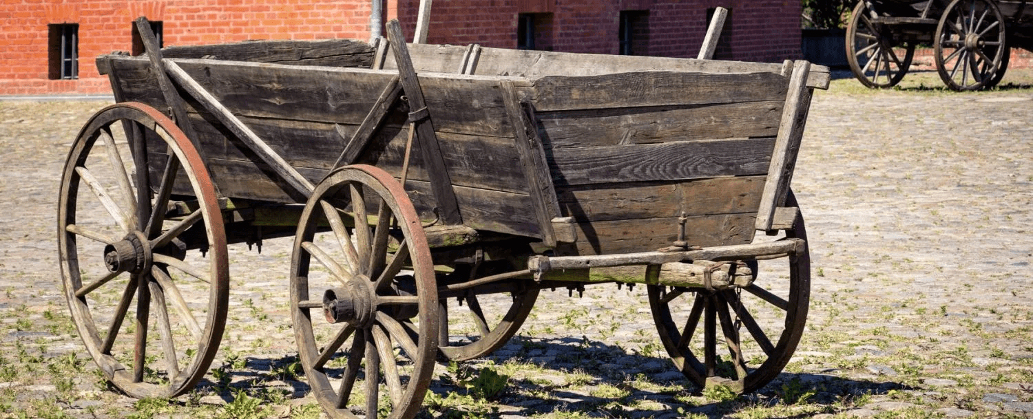A weathered wooden cart with large wheels, sitting on a cobblestone surface.
